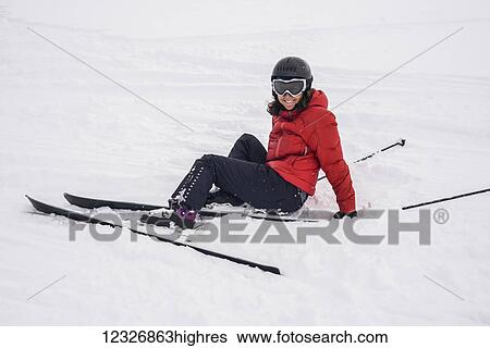 Stock Photograph - A skier in a red coat sitting in the snow; Whistler, British Columbia, Canada. Fotosearch