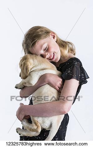 Stock Photograph - A smiling young girl hugs a Labrador puppy against a white background; Anchorage, Alaska, United States of America. Fotosearch