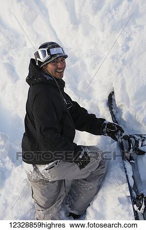 Stock Photograph - A snowboarder poses while climbing steep terrain in deep snow with his snowboard; Alaska, United States of America. Fotosearch