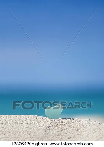 Stock Photograph - A turquoise heart shaped sea glass in the sand at the beach; Honolulu, Oahu Hawaii, United States of America. Fotosearch