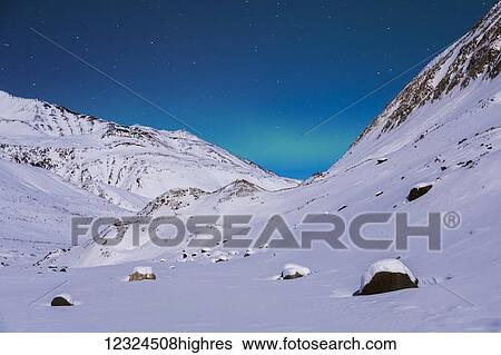 Stock Photograph - A very faint band of aurora stretches between the mountains in a remote location in the Alaska Range in winter, near Augustana Glacier; Alaska, United States of America. Fotosearch