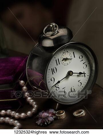 Stock Photograph - A vintage clock on a bedside table with a string of pearls, brooch and rings; Alberta, Canada. Fotosearch
