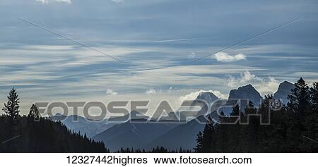 A wide angle view of a winter landscape of the rocky mountain peaks along the highway in Banff National Park, with misty daytime clouds painting the horizon and the silhouette of trees in the foreground; Lake Louise, Alberta, Canada View Large Photo Image Stock Photograph - A wide angle view of a winter landscape of the rocky mountain peaks along the highway in Banff National Park, with misty daytime clouds painting the horizon and the silhouette of trees in the foreground; Lake Louise, Alberta, Canada. Fotosearch