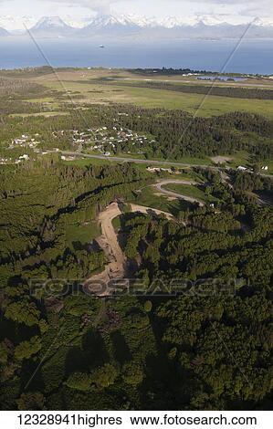 Stock Photograph - A winding road through a forest in the foreground with a view of the Kenai Mountains and Kachemak Bay in the background; Homer, Alaska, United States of America. Fotosearch