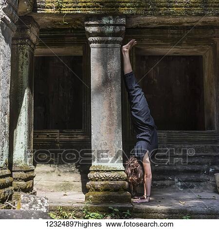 Stock Photograph - A woman does a hand stand at Ta Prohm Temple; Krong Siem Reap, Siem Reap Province, Cambodia. Fotosearch