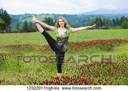 Stock Photograph - A woman does yoga in a field of wildflowers with mountains in the background; Oregon, United States of America. Fotosearch