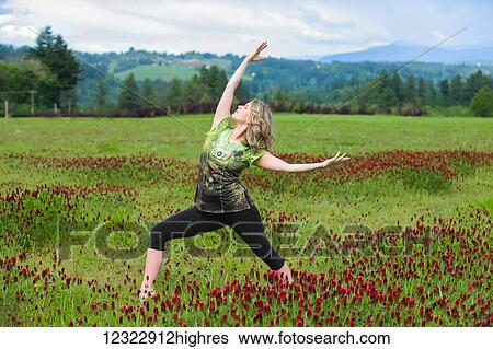 Stock Photograph - A woman does yoga in a field of wildflowers with mountains in the background; Oregon, United States of America. Fotosearch