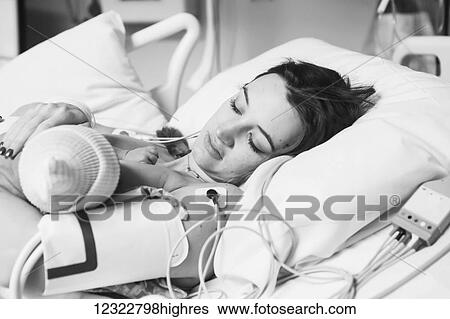 Stock Photograph - A woman lays in a hospital bed with her newborn baby; Oregon, United States of America. Fotosearch