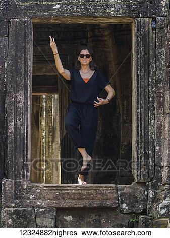 Stock Photograph - A woman stands doing a yoga pose in an opening of Bayon Temple, Angkor Thom; Krong Siem Reap, Siem Reap Province, Cambodia. Fotosearch