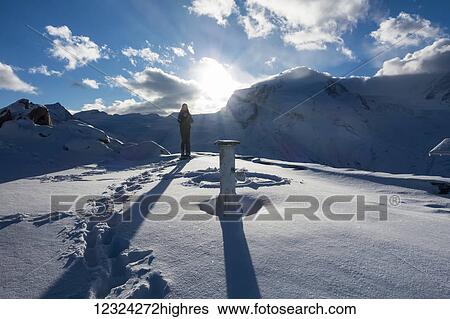 Stock Photograph - A woman stands in the snow at sunrise on Gornergrat summit, Monte Rosa, Pennine Alps; Zermatt, Valais, Switzerland. Fotosearch