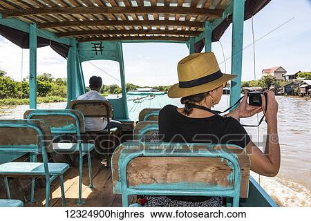 Stock Photograph - A woman takes a picture of Kampong Phluk, a floating village, from a boat as it tours down a river; Siem Reap Province, Cambodia. Fotosearch