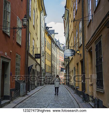Stock Photograph - A woman walking down a street between colourful retail and residential buildings; Stockholm, Sweden. Fotosearch