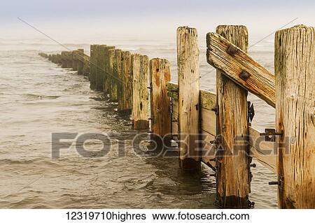 Stock Photograph - A wooden fence leading out in the ocean water; Berwick, Northumberland, England. Fotosearch