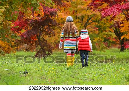 A young boy and girl wearing rubber boots and colourful clothing walk across a field towards trees in bright autumn colours; Oregon, United States of America View Large Photo Image Stock Photograph - A young boy and girl wearing rubber boots and colourful clothing walk across a field towards trees in bright autumn colours; Oregon, United States of America. Fotosearch