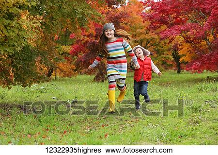 A young boy and girl wearing rubber boots and colourful clothing run across a field holding hands with trees in bright autumn colours in the background; Oregon, United States of America View Large Photo Image Stock Photograph - A young boy and girl wearing rubber boots and colourful clothing run across a field holding hands with trees in bright autumn colours in the background; Oregon, United States of America. Fotosearch