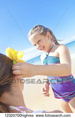 Stock Photograph - A young girl putting a tropical flower into her mother's hair on the beach; Hawaii, United States of America. Fotosearch