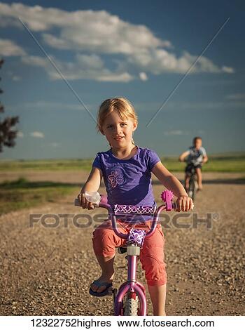A young girl riding her bicycle down a gravel road with her brother riding behind; Herschel, Saskatchewan, Canada View Large Photo Image Stock Photograph - A young girl riding her bicycle down a gravel road with her brother riding behind; Herschel, Saskatchewan, Canada. Fotosearch