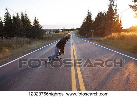 A young man skateboarding down a road at dusk; Homer, Alaska, United States of America View Large Photo Image Stock Photograph - A young man skateboarding down a road at dusk; Homer, Alaska, United States of America. Fotosearch