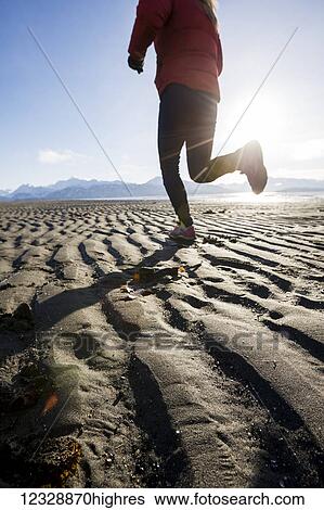Stock Photograph - A young woman jogs on the wet beach; Homer, Alaska, United States of America. Fotosearch