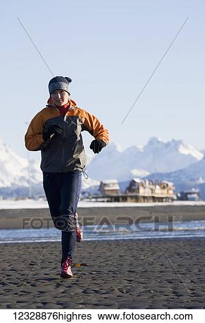 Stock Photograph - A young woman jogs on the wet beach; Homer, Alaska, United States of America. Fotosearch