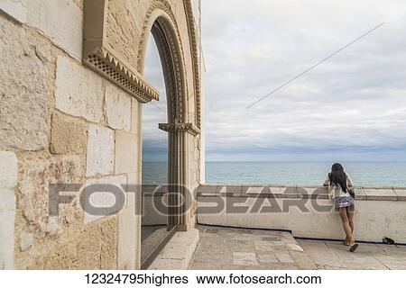 A young woman looks out over a wall to the ocean at Maricel Palace; Sitges, Barcelona province, Spain View Large Photo Image Stock Photograph - A young woman looks out over a wall to the ocean at Maricel Palace; Sitges, Barcelona province, Spain. Fotosearch
