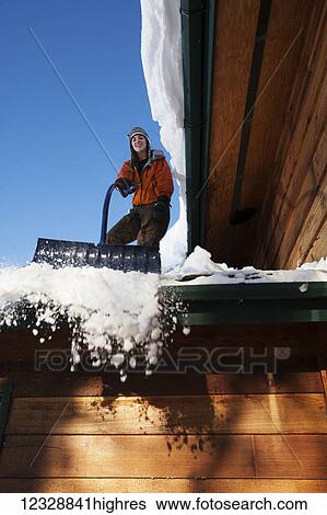 Stock Photograph - A young woman removes snow from the roof of her house; Homer, Alaska, United States of America. Fotosearch