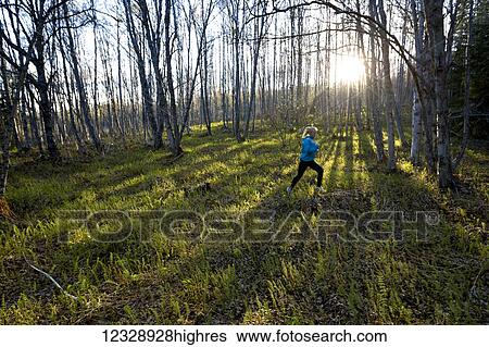 Stock Photograph - A young woman running across the plants of the forest floor in a forest; Homer, Alaska, United States of America. Fotosearch