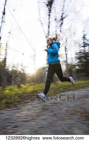 Stock Photograph - A young woman running on a trail in a forest; Homer, Alaska, United States of America. Fotosearch