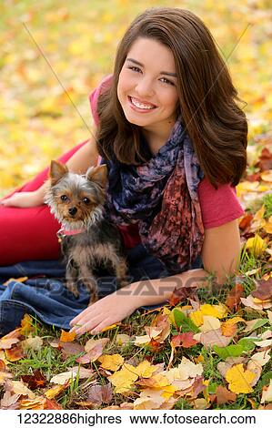 Stock Photograph - A young woman sits with her dog on the leaf covered grass in autumn; Oregon, United States of America. Fotosearch