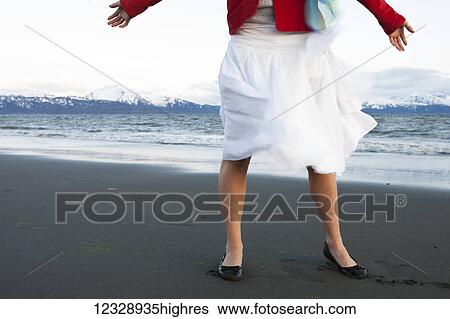 A young woman standing on a beach at the water's edge with arms outstretched wearing a white skirt and red jacket; Homer, Alaska, United States of America View Large Photo Image Stock Photograph - A young woman standing on a beach at the water's edge with arms outstretched wearing a white skirt and red jacket; Homer, Alaska, United States of America. Fotosearch