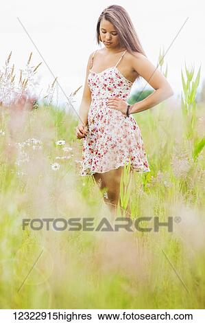 Stock Photograph - A young woman stands looking contemplative in a field of wildflowers and tall grasses; Oregon, United States of America. Fotosearch