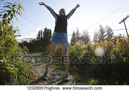 A young woman stands on a trail in a running outfit looking up to the sky with arms raised; Homer, Alaska, United States of America View Large Photo Image Stock Photograph - A young woman stands on a trail in a running outfit looking up to the sky with arms raised; Homer, Alaska, United States of America. Fotosearch