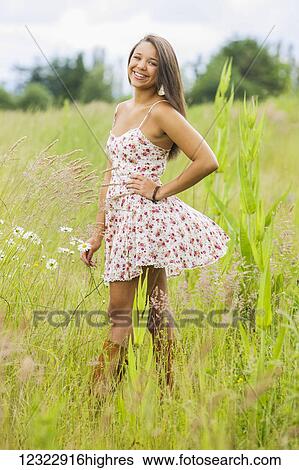 Stock Photograph - A young woman stands smiling in a field of wildflowers and tall grasses; Oregon, United States of America. Fotosearch