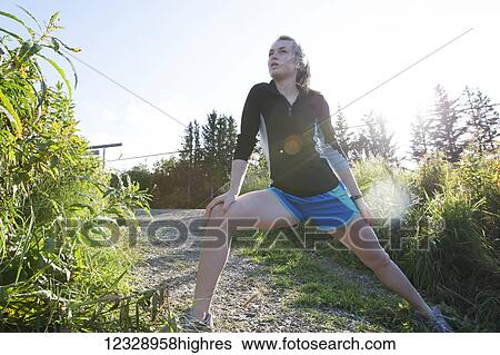 Stock Photograph - A young woman stretching on a trail before a run; Homer, Alaska, United States of America. Fotosearch