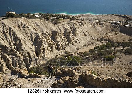 Stock Photograph - A young woman takes photographs from a trail in the Dead Sea region, with the Dead Sea in the background; South District, Israel. Fotosearch