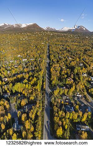 Stock Photograph - Aerial view of the hillside neighbourhood homes in Anchorage, snow covering the peaks of the Chugach Mountains in the background, autumn coloured trees filling the city, South-central Alaska; Alaska, United States of America. Fotosearch