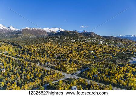 Stock Photograph - Aerial view of the hillside neighbourhood homes in Anchorage, snow covering the peaks of the Chugach Mountains in the background, autumn coloured trees filling the city, South-central Alaska; Alaska, United States of America. Fotosearch