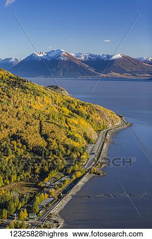 Stock Photograph - Aerial view of the Seward Highway running South along the Turnagain Arm, snow covering the Kenai Mountains in the background, autumn coloured trees filling the hillsides, South-central Alaska; Anchorage, Alaska, United States of America. Fotosearch