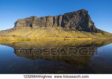 Stock Photograph - Ancient volcanic cliff lining the South Coast of Iceland; Iceland. Fotosearch