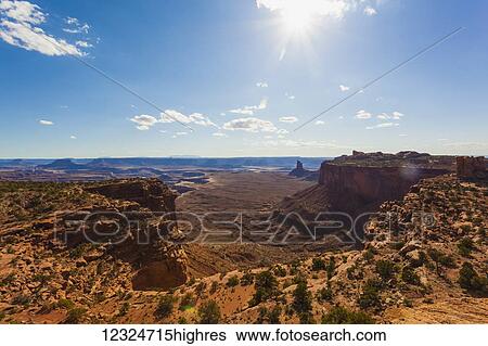 Stock Photograph - Arid landscape of cliffs and rugged terrain under a blue sky with cloud and sunlight; Utah, United States of America. Fotosearch