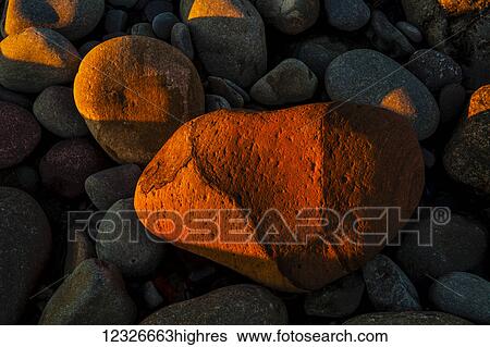 Stock Photograph - Beach stones on the shore of Cow Bay catch the last direct sunlight of the setting sun; Cow Bay, Nova Scotia, Canada. Fotosearch