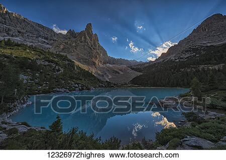 Stock Photograph - Beams of sunlight shine through the late afternoon sky over Sorapiss Lake in the Italian Dolomites; Cortina, Italy. Fotosearch