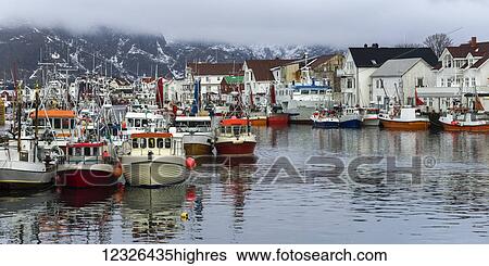 Stock Photograph - Boats in the harbour and buildings on the shore with low cloud hanging overhead; Lofoton Islands, Nordland, Norway. Fotosearch