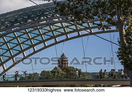 Stock Photograph - Bridge of Peace, a bow-shaped pedestrian bridge over the Mtkvari (Kura) River and Metekhi Church; Tbilisi, Georgia. Fotosearch