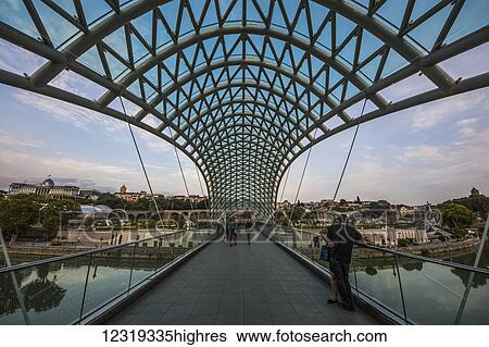 Stock Photograph - Bridge of Peace, a bow-shaped pedestrian bridge over the Mtkvari (Kura) River and Metekhi Church; Tbilisi, Georgia. Fotosearch