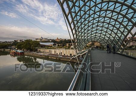 Stock Photograph - Bridge of Peace, a bow-shaped pedestrian bridge over the Mtkvari (Kura) River; Tbilisi, Georgia. Fotosearch