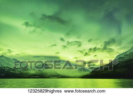 Stock Photograph - Bright green Aurora Borealis dances over Upper Trail Lake, the Kenai Mountains in the background, Moose Pass, Kenai Peninsula, South-central Alaska; Alaska, United States of America. Fotosearch
