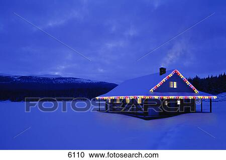 Stock Image - Cabin with Christmas lights and snowy backdrop. Fotosearch