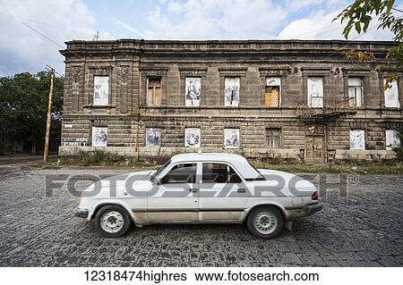Stock Photograph - Car driving by a building on Abovyan Street where the windows are filled by black and white portraits of people; Gyumri, Shirak Province, Armenia. Fotosearch