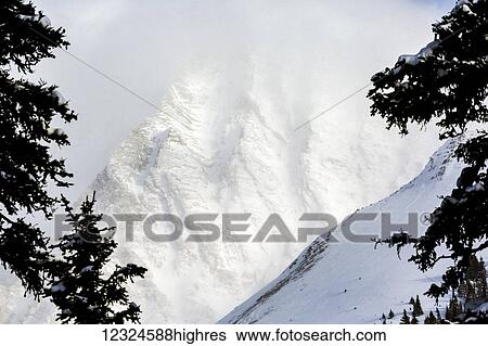 Close up of a snow covered mountain face framed with evergreen trees; Kananaskis Country, Alberta, Canada View Large Photo Image Stock Photograph - Close up of a snow covered mountain face framed with evergreen trees; Kananaskis Country, Alberta, Canada. Fotosearch